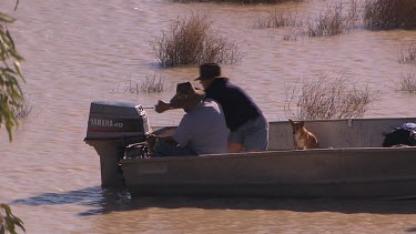 Two people (man and woman) fishing in tinny boat with outboard motor. They have a dog with them. They are on very shallow waters of flooded desert plain. Starting engine of outboard motor.