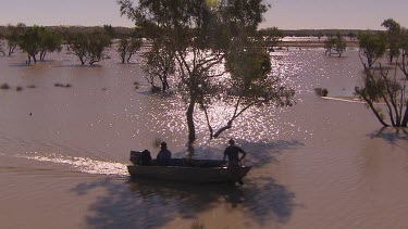 Three people fishing in tinny boat with outboard motor. They have a dog with them. They are on very shallow waters of flooded desert plain. High Angle. Sun reflecting glistening on water, people in si...