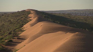 Simpson Desert. Sand dunes long shot like a spine.  Ripples of sand on sand dune from wind. Desert plain in flood background