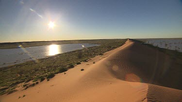 Simpson Desert. Sand dunes long shot like a spine.  Ripples of sand on sand dune from wind. Desert plain in flood background