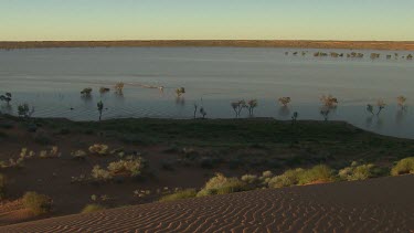 Zoom out from people boating in tinny with outboard motor across flooded desert plain. Simpson Desert