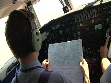 Over shoulder shot of pilots in cockpit of small plane, navigating using a map.