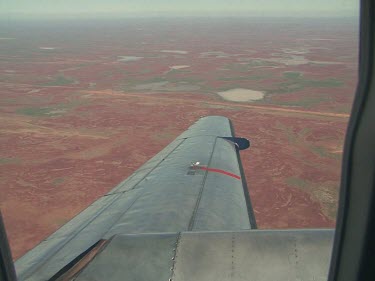 Desert below, close up of plane wing. Lake Eyre, Simpson Desert flooded, patches of green