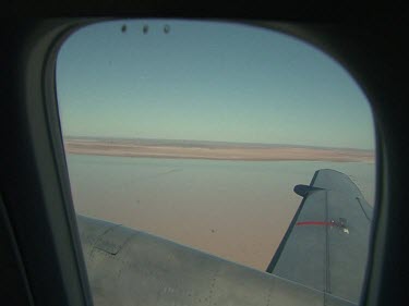 Desert below, close up of plane wing.  Lake Eyre, Simpson Desert flooded, patches of green
