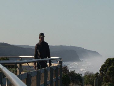 One man standing overlooking the Ocean, waves, spray, cliffs in background.