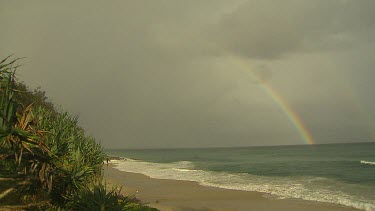 Beach with rainbow over ocean.