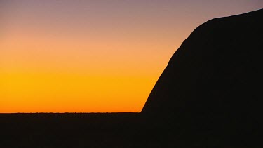 Sunset Uluru, the curve of the rock in silhouette against a red sky