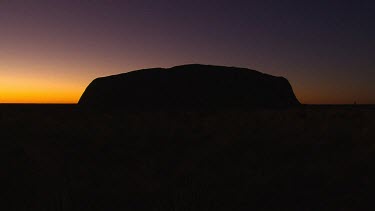 Sunset medium wide shot Uluru in silhouette