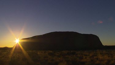 Sunrise. Sun rising behind curve of rock of Uluru.