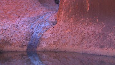 Water pool at base of rock. Wet rock is black. Water flowing in desert.