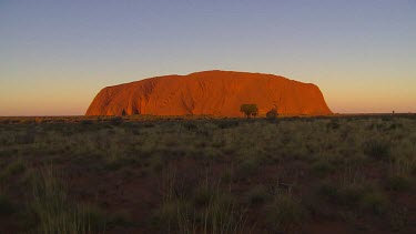 Typical iconic wide shot of Uluru late afternoon sunlight Uluru appears as very red rock on horizon.