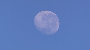Full moon in blue daylight sky.