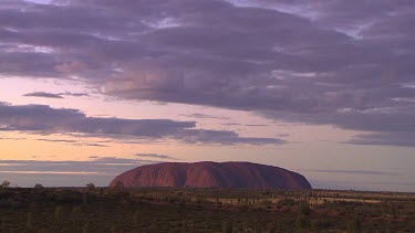 Typical iconic wide shot of Uluru clouded sky, darker hues.