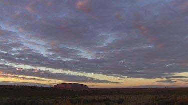 Typical iconic wide shot of Uluru time lapse clouds moving across sky.