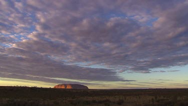 Typical iconic wide shot of Uluru time lapse clouds moving across sky.