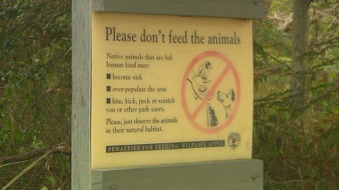 Conservation sign says Please do not feed the animals, penalties for feeding wildlife apply Native animals that are fed human food may become sick, over-populate the area; bite kick peck or scratch yo...