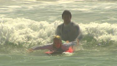 Young woman learning to surf falls off surfboard