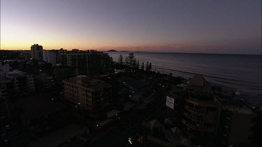 High angle wide establishing shot of Queensland Sunshine coast town Mooloolaba. Shows hotels and beach with palm trees, holiday atmosphere. Sunset.