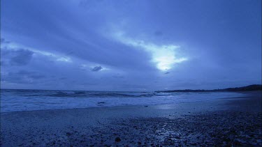 Wide Shot. Waves lapping on beach evening low light.