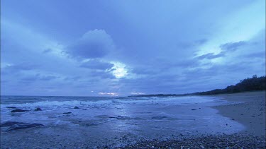 Wide Shot. Pebble beach with rocks in evening light. Sea and sky. Sun set in distance, horizon.