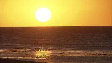 Lock off shot Calm beach at sunset. Big yellow sun in orange sky. Sun setting.