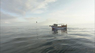 Fishermen reeling in basket. Fishing boat. Blue grey sky, silvery sheen on water. Reflection of light.