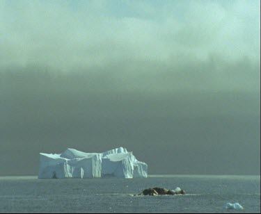 Iceberg in ocean. Tabular iceberg. Stormy grey skies overhead.