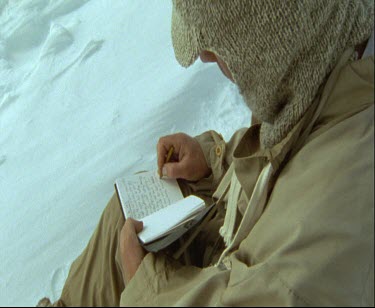 One man camping in snowy white landscape Close up. He is writing in a notebook.