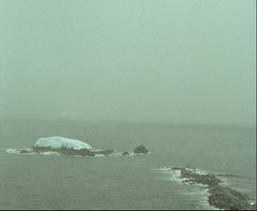 Stormy seas, snowing and raining ice capped rock islands