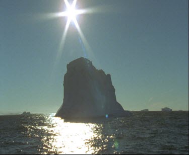 Silhouette backlit iceberg with bright sunshine in background.