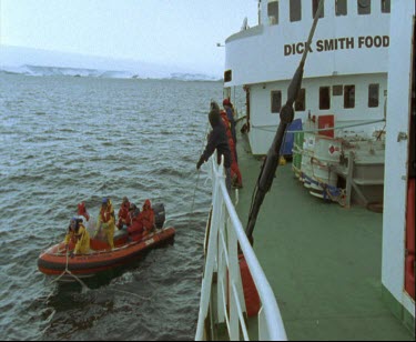 Men climbing aboard zodiac inflatable dinghy  setting off for land. Ice sheet ice shelf in background.
