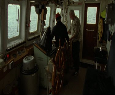 Interior of ship with steering wheel helm. Captain discusses coruse of navigation.