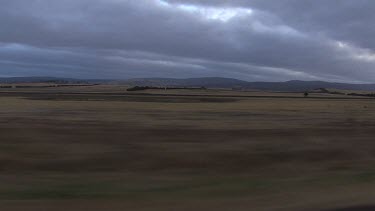 Tracking shots driving past rural landscape. Grassy fields Heavy dark grey rain clouds in sky.