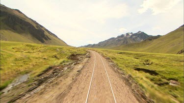 Shot from very back of a train following the rails with the Andes in the background