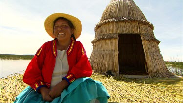 A local of Lake Titicaca, sitting on her hand made reed island with a hut behind her