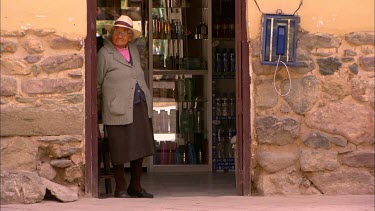 Old woman standing in a shop doorway with drinks behind her