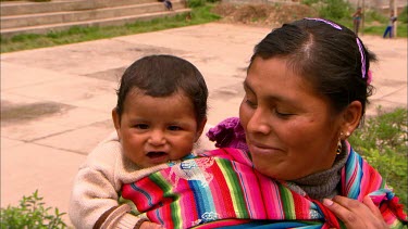Peruvian woman and her child in a traditional sling on her back.