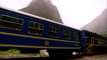Side on of blue and yellow Andean Explorer train moving through misty mountains