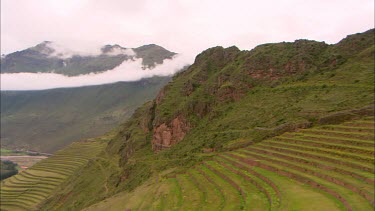 Panning shot of terraced hills looking down at Ollantaytambo in Peru with cloud covered mountains in the background