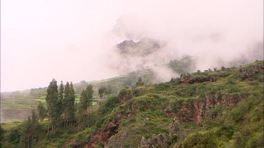 Mountain peaks covered by clouds with smaller tree lined ridge in the foreground