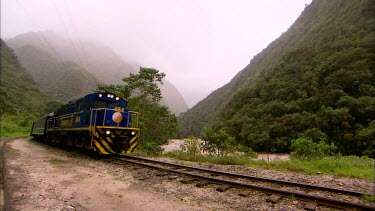 A train passes by the Urubamba river, travelling through a misty valley