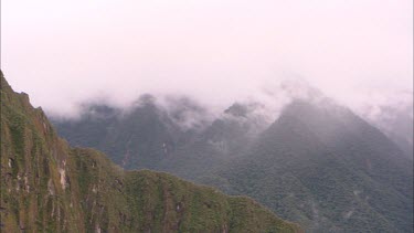 Panning across the cloud covered mountaind surrounding Machu Picchu