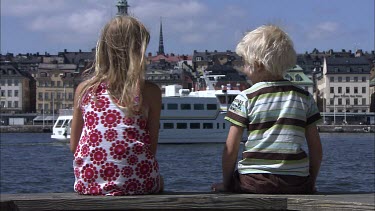 Two kids sitting and talking by the water. Gamla Stan, The Old Town, Stockholm. A ferry in the background.