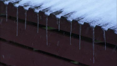 Heavy snow fall, icy roof top edge and red wall as a background