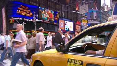 Pedestrians walk across road while taxi waits and looks at advertising. LCD billboards.