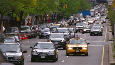 New York avenue with trees, traffic lights. Cars and yellow cabs.
