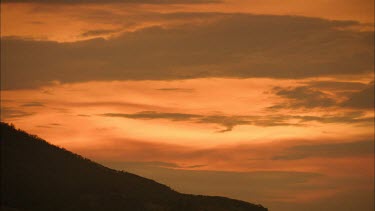 Sunset sky, clouds. Mountain in foreground in dark silhouette. Dramatic
