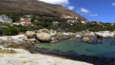 pan over Boulders beach, rocky shoreline, houses in BG