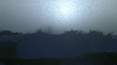 Night, a big stormy wave crashes against a rock. Lightening crashes on sea