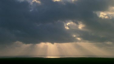 Rising sun pierces clouds shines onto sea